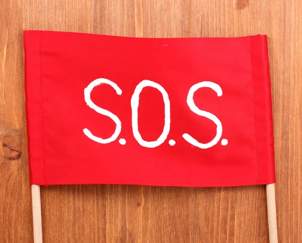 SOS signal skrivit på rött tyg på trä bakgrund — Stockfoto