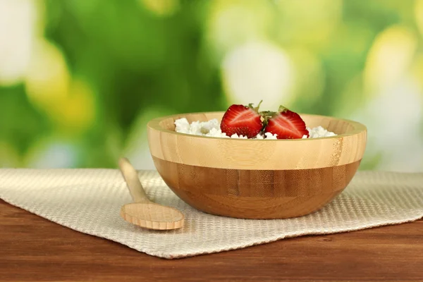 Cottage kaas met aardbei in houten kom met houten lepel op beige servet op houten tafel op groene achtergrond — Stockfoto