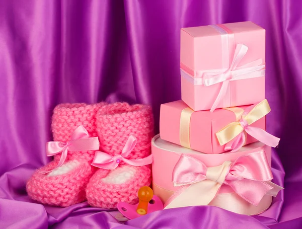 Rosa baby stövlar, napp, gåvor på silk bakgrund — Stockfoto