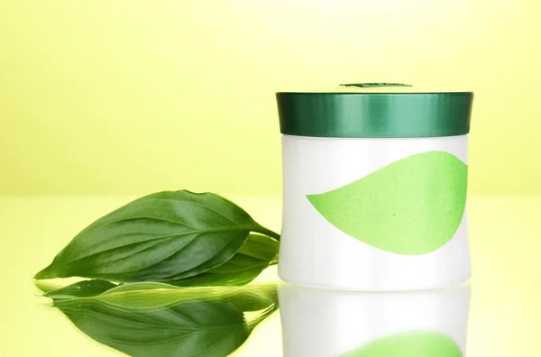 Tarro de crema con hojas verdes sobre fondo verde — Foto de Stock
