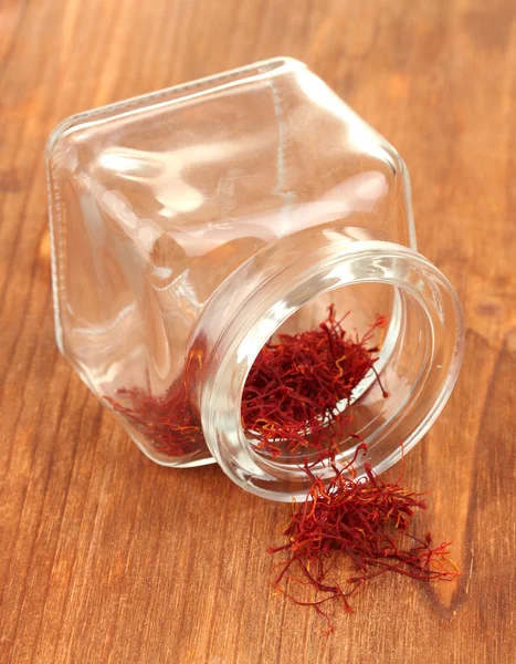 Stigmas of the saffron poured out a glass jar on wooden background close-up — Stock Photo, Image