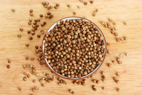 Heap coriander seeds in bowl on wooden background close-up — Stock Photo, Image