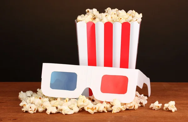 Popcorn a kino brýle na dřevěný stůl na hnědé pozadí — Stock fotografie