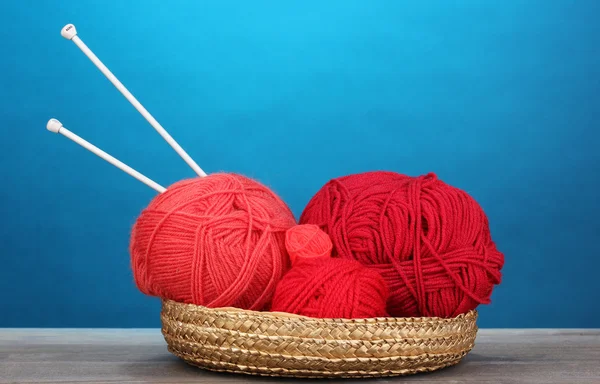 Red knittings yarns in basketon on wooden table on blue background — Stock Photo, Image