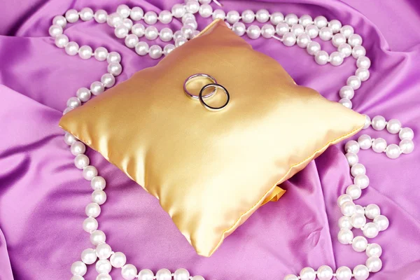Anéis de casamento no travesseiro de cetim no fundo pano roxo — Fotografia de Stock