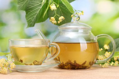 Teapot and cup with linden tea and flowers on wooden table in garden clipart