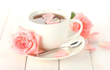 Cup of tea with roses on white wooden table clipart