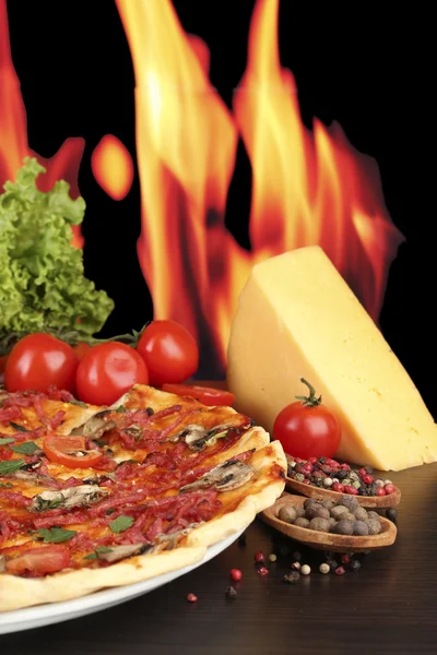 Güzel pizza, salam, domates ve baharatlar alev arka plan üzerinde ahşap tablo — Stok fotoğraf
