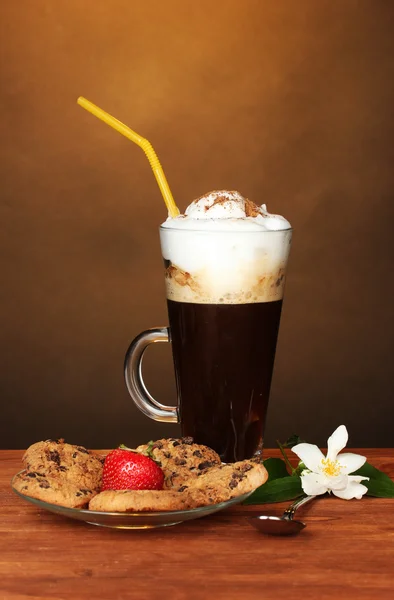 Ποτήρι καφέ κοκτέιλ με τα cookies και η φράουλα στο πιατάκι και λουλούδια σε καφέ φόντο — Φωτογραφία Αρχείου