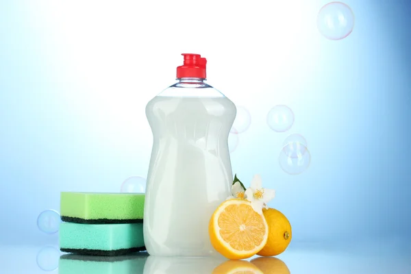 Folyékony mosogatószer, szivacsok és a citrom, a virágok, kék háttérrel — Stock Fotó