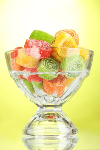 Kleurrijke gelei snoepjes in in glazen kom op groene achtergrond — Stockfoto