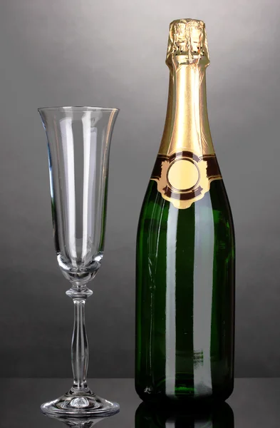 Láhev šampaňského a pohár na šedém pozadí — Stock fotografie