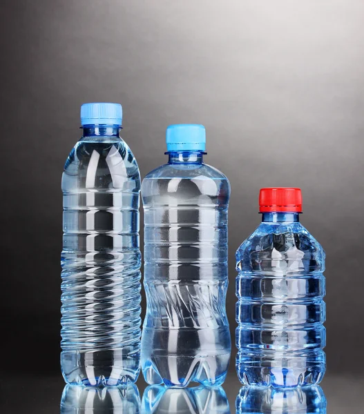 Plastikflaschen mit Wasser auf grauem Hintergrund — Stockfoto