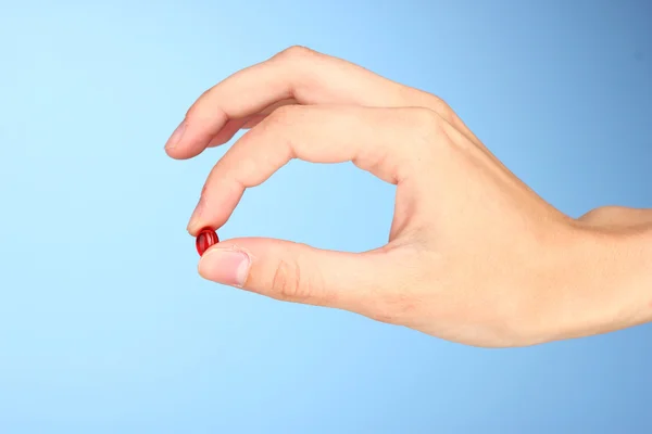 Kvinnans hand som håller ett rött piller på blå bakgrund närbild — Stockfoto