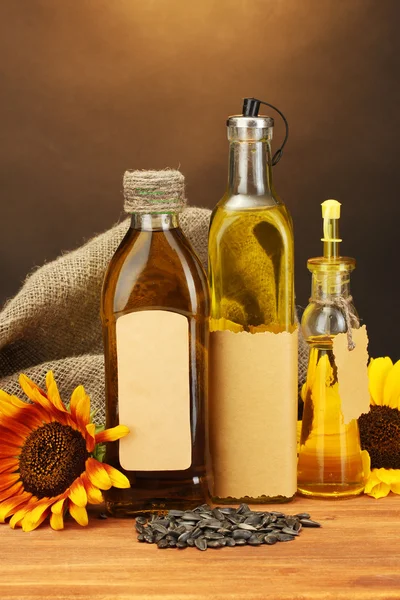 Олія в пляшках, соняшниках і насіннях, на дерев'яному столі на коричневому фоні — стокове фото
