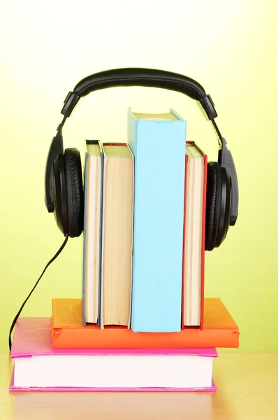 Sluchátka na knihy o dřevěný stůl na zeleném pozadí — Stock fotografie