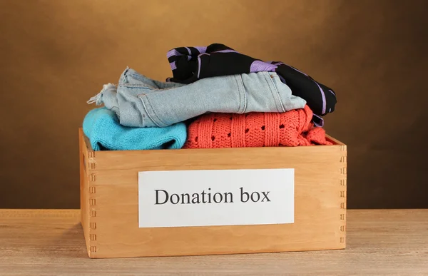 Donation box with clothing on brown background close-up — Stock Photo, Image