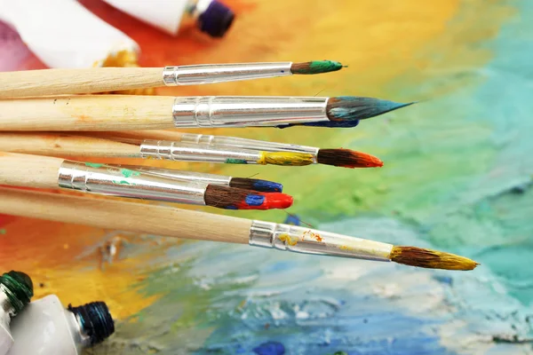 Acrylic paint, paint tubes and brushes on wooden palette — Stock Photo, Image
