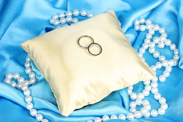 Обручальные кольца на атласной подушке на синем фоне ткани — стоковое фото