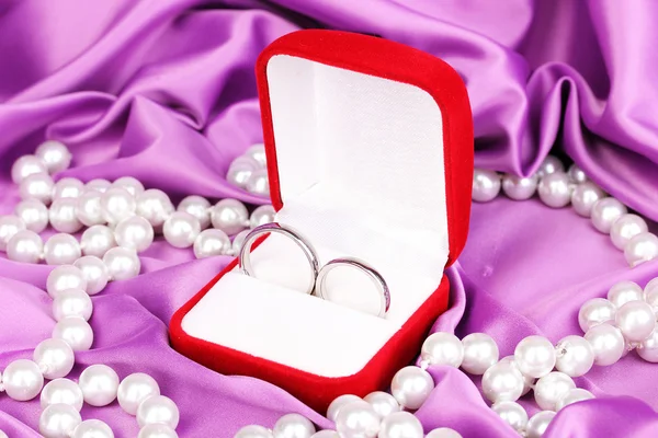 Anéis de casamento em caixa vermelha no fundo pano roxo — Fotografia de Stock