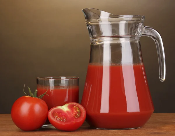 Tomato juice in pitcher and glass on wooden table on brown background — Stock Photo, Image