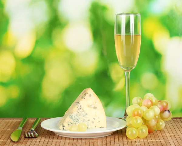 Käse mit Schimmel auf dem Teller und einem Glas Wein auf grünem Hintergrund Nahaufnahme — Stockfoto