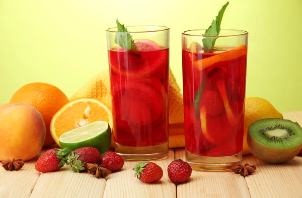 Refreshing sangria in glasses with fruits, on wooden table, on green background — Stock Photo, Image