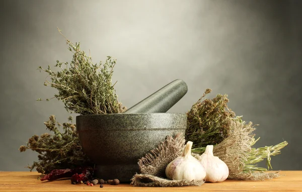 Ervas secas em argamassa e legumes, sobre mesa de madeira sobre fundo cinzento — Fotografia de Stock