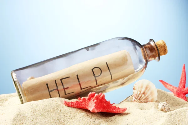 Glass bottle with note inside on sand, on blue background — Stock Photo, Image