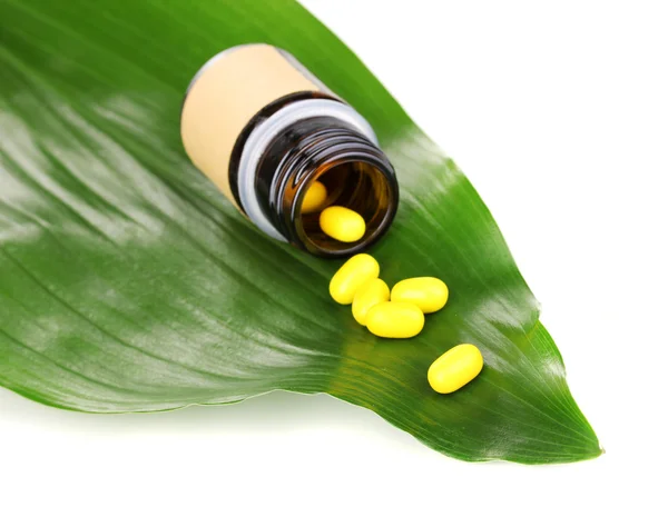 Tabletten op groene blad met fles geïsoleerd op wit — Stockfoto