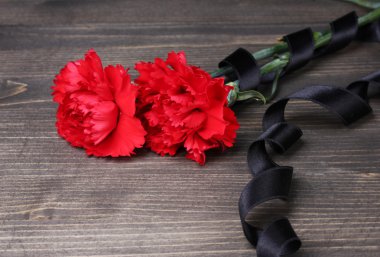 Carnations and black ribbon on grey wooden background clipart