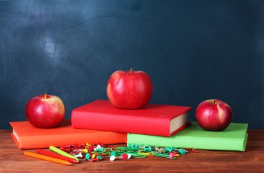 Composition of books, stationery and an apples on the teacher's desk in the background of the blackboard clipart
