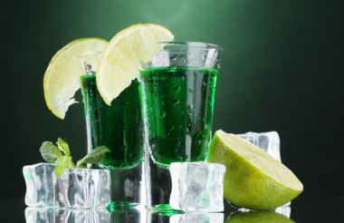 Two glasses of absinthe, lime and ice on green background clipart