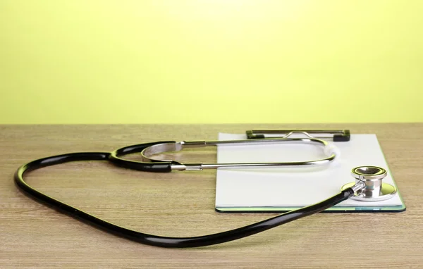 Estetoscopio médico y portapapeles sobre mesa de madera sobre fondo verde — Foto de Stock