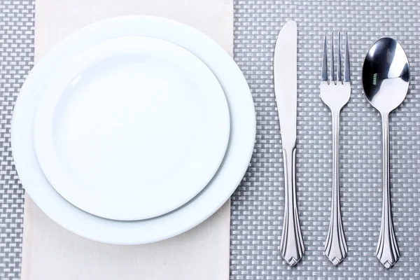 Placas brancas vazias com garfo, colher e faca em uma toalha de mesa cinza — Fotografia de Stock