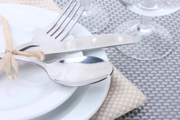 Bílé prázdné talíře, vidličku, lžíci a nůž převázaná stuhou a brýle na šedé ubrus — Stock fotografie