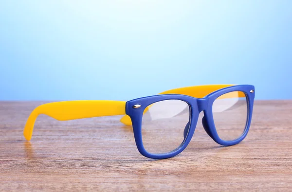 Krásné barevné brýle na dřevěný stůl na modrém pozadí — Stock fotografie