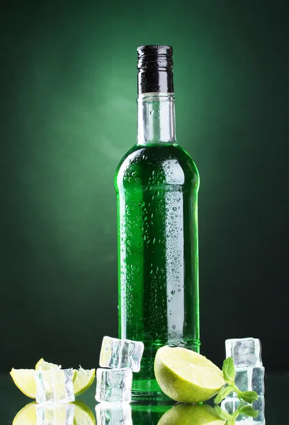 Бутылка абсента с лаймом и льдом на зеленом фоне — стоковое фото
