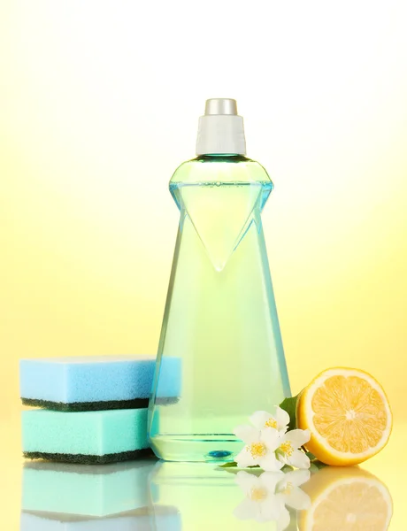 Жидкость для мытья посуды с губками и лимон с цветами на желтом фоне — стоковое фото