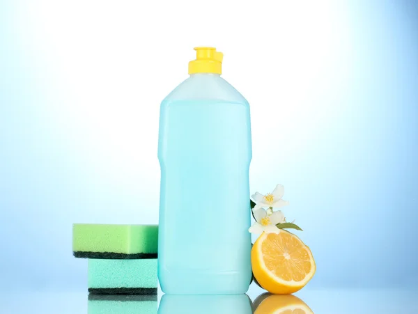 Spülmittel mit Schwämmen und Zitrone mit Blumen auf blauem Hintergrund — Stockfoto