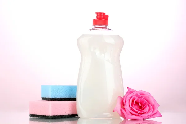 Liquido per lavastoviglie con spugne e fiori su sfondo rosa — Foto Stock