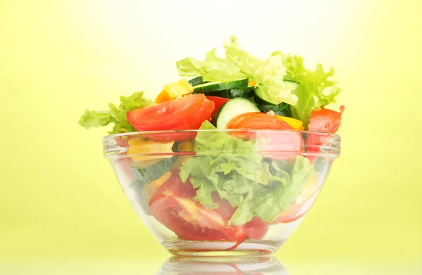 Салат из свежих овощей в прозрачной миске на зеленом фоне — стоковое фото