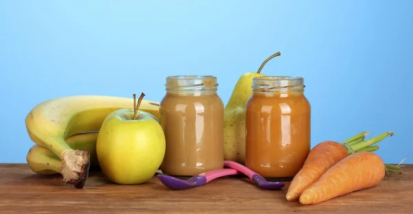 Jar met fruit en groenten babyvoeding, lepel en vruchten en groenten op kleurrijke servet op blauwe achtergrond — Stockfoto