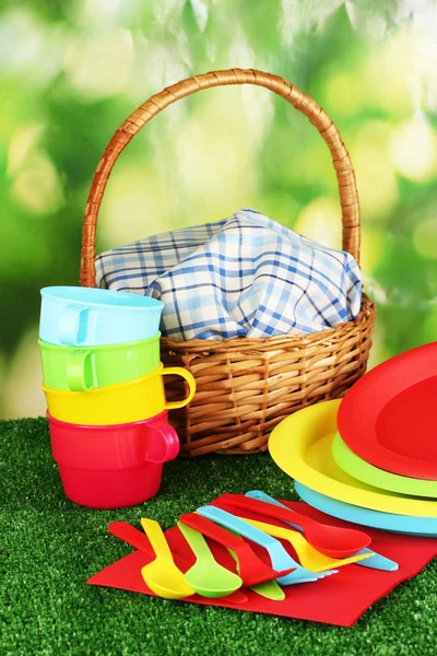 stock image Bright plastic disposable tableware and picnic basket on the lawn on colorful background