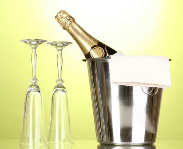 Bottiglia di champagne in secchio con ghiaccio e bicchieri su sfondo verde — Foto Stock