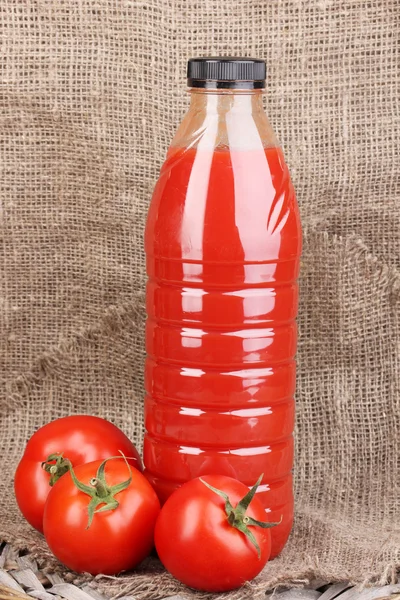 Tomato juice in bottle on sackcloth background — Stock Photo, Image