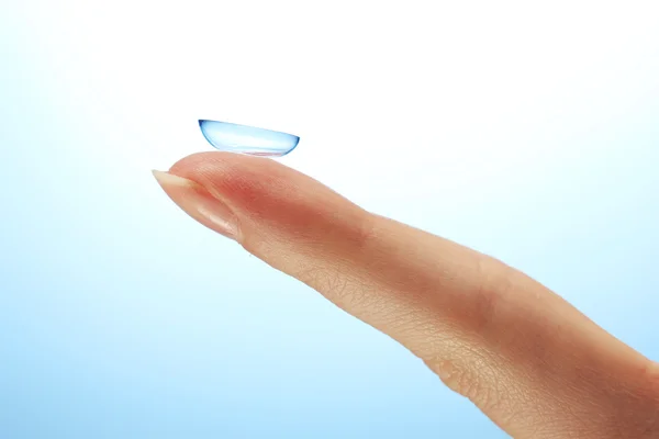 Kontaktlinse am Finger auf blauem Hintergrund — Stockfoto