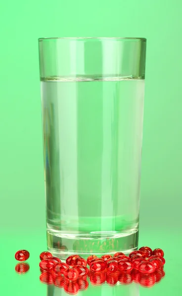 A glass of water and pills on green background close-up — Stock Photo, Image