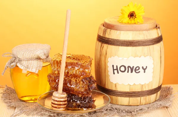 Barrel of honey and honeycomb on wooden table on orange background — Stock Photo, Image