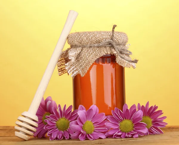 Süßer Honig im Glas mit Nieselregen auf Holztisch auf gelbem Hintergrund — Stockfoto